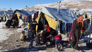 Syrische Flüchtlinge kochen und essen vor ihren Zelten.