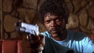 Samuel L. Jackson in einem hellblauen T-Shirt. Er zielt mit einer Pistole auf eine ihm gegenübersitzende Person, die nicht sichtbar ist. Sein BLick ist grimmig.