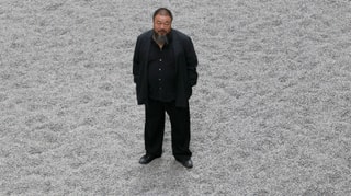 Künstler Ai Weiwei auf grauem Untergrund stehend.