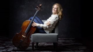 Eine Frau mit blonden Haaren sitzt auf einem Sessel und hält ein Cello.