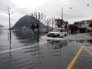 Ein Fahrzeug fährt über eine überflutete Strasse im Bereich des Luganer Sees.