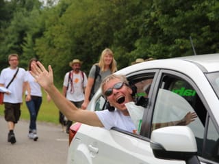 Reto Scherrer winkt fröhlich aus einem Auto, das gerade die Wandergruppe überholt.