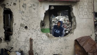 Ein Mann schaut durch ein Loch in einem zerbombte Haus. 