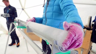 Eine Person nimmt aus einer langen Metallröhre einen länglichen Eiszylinder