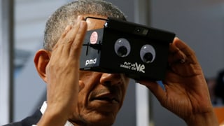 Barack Obama ein Gerät vor den Augen haltend.