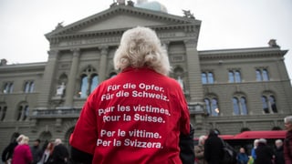 Eine Frau mit weissen Haaren von hinten, auf ihrem roten T-Shirt steht «Für die Opfer, für die Schweiz».