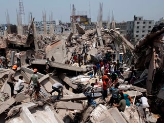 Männer klettern über zerbrochene Beton-Bauelemente des zusammengestürzten Gebäudes.