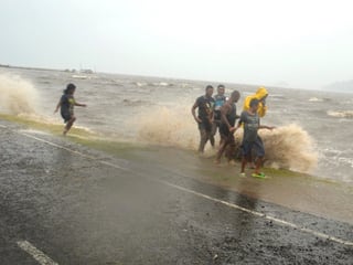 Menschen gehen am Rande einer Strasse, als grosse Wellen ans Ufer preschen