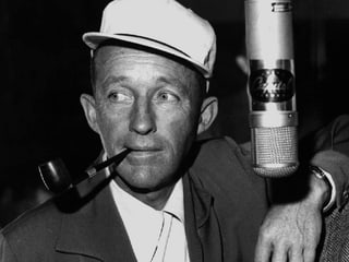 Ein Mann mit weissem Hut und Tabakpfeife vor einem Mikrofon.