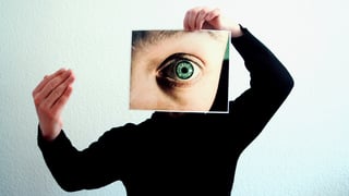 Ein Mensch hält ein Foto eines weit geöffneten Auges vor sein Gesicht. 