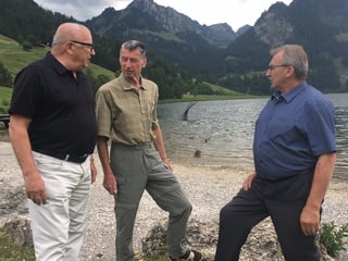 Drei Männer stehen auf einem Kiesstrand.