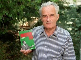 Kurt Meier mit einem Buch in der Hand, das seine Geschichte beschreibt.