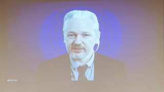 Julian Assange auf einer Leinwand mit UNO-Wappen im Hintergrund