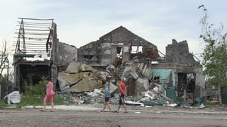 Drei Leute laufen vor einem ausgebombten Haus vorbei.