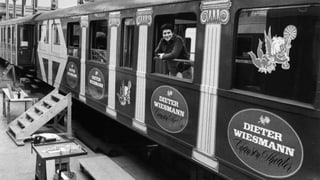 Schwarz-Weiss-Fotografie mit einem Mann der aus dem Fenster eines Zugwaggons schaut.
