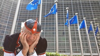 Symbolbild: Ein Mann in Schweizer Tracht sitzt vor dem Gebäude der EU-Kommission in Brüssel, hat das Kinn in die Hände gestützt und scheint zu schlafen.