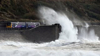 Ein Zug fährt entlang der englischen Küste und wird von einer hohen Welle getroffen