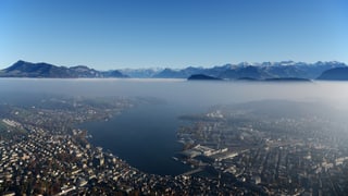 Blick aus der Luft auf die Stadt Luzern. Über der Dunstschicht das Alpenpanorama und blauer Himmel.