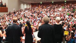 Blick von der Orchesterbühne ins Publikum, dass eine Standingovation gibt und Herzchen auf Plakaten in die Höhe halten. Blick von der Orchesterbühne ins Publikum, dass eine Standingovation gibt und Herzchen auf Plakaten in die Höhe halten.