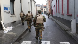 Vier Polizisten durchkämmen eine Strasse in Molenbeek, Grafitti links an der Wand.
