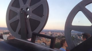 Es ist eine alte Filmrolle zu sehen vor dem Panorama der Stadt Basel.