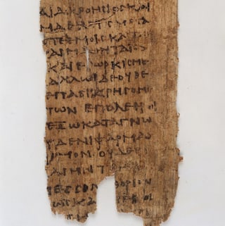 Ein zerfetztes Stück mit schwarzer, griechischer Schrift.