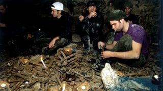 Jugendliche sitzen auf Knochenhaufen und zünden Kerzen an.