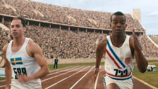 Filmstill: Ein schwarzer und ein weisser Läufer duelleiern sich in einem riesigen Stadion.