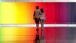 Ein Paar vor einem regenbogenfarbigen Gemälde.