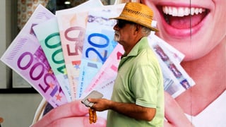 Ein Mann geht an einem Poster vorbei, auf dem eine Werbung mit Euro-Noten zu sehen ist. 