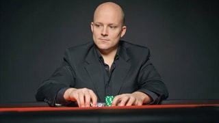 Rino Mathis in einem schwarzen Anzug mit Poker Chips in der Hand. 