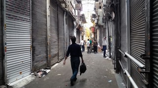 Einzelne Personen in einer Gasse, in der die Rolläden der Shops unten sind. Einzelne Personen in einer Gasse, in der die Rolläden der Shops unten sind.