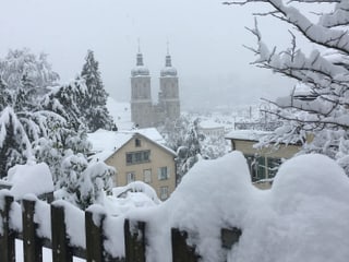 Blick über verschneiten Zaun zum St. Galler Dom, alles liegt unter einem dicken Schneekleid.