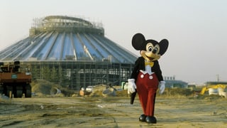 Ein Mickey-Maus-Maskottchen auf einer Baustelle, wo gerade ein neuer Themenpark entsteht.