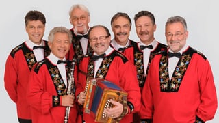 Gruppenbild mit den sieben Musikanten, die alle rote Sennenkutten tragen.