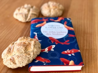 Der  Roman «Die zehn Lieben von Nishino» von Hiromi Kawakami liegt auf einem Tisch, angelehnt am Buch ein japanisches  Melonpan - ein weiche Biskquitkugel.