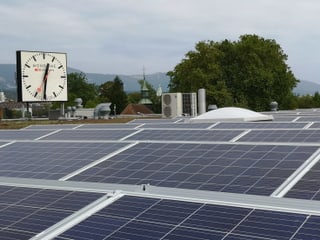 Solaranlage auf einem Flachdach. Dahinter eine grosse Uhr. Solaranlage auf einem Flachdach. Dahinter eine grosse Uhr.