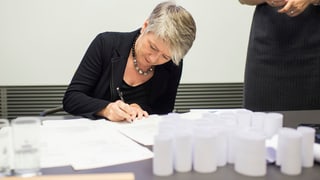 Jacqueline Fehr setzt ihre Unterschrift auf ein Dokument, vor ihr auf dem Tisch stehen die aufgerollten Nationalratslisten.