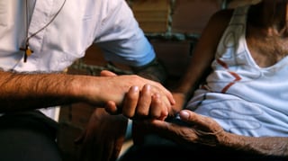 Ein Mann mit Christus-Kreuz-Halskette reicht einer anderen Person die Hand Ein Mann mit Christus-Kreuz-Halskette reicht einer anderen Person die Hand
