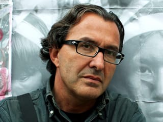 Ein Mann mit Brille und halblangem, gewelltem Haar lehnt an eine Mauer. Er ist braungebrannt. Ein Mann mit Brille und halblangem, gewelltem Haar lehnt an eine Mauer. Er ist braungebrannt.