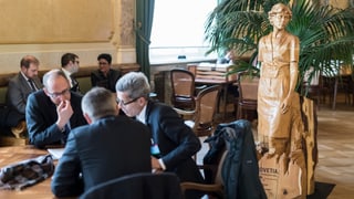 Männer in Anzügen sitzen an Tischen in der Lobby des Bundeshauses und sprechen miteinander.