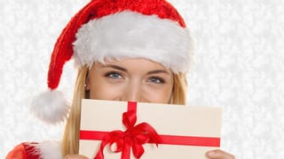 Eine Frau mit Weihnachtsmann-Mütze hält sich einen Geschenkgutschein vors Gesicht.