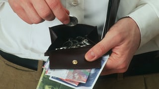 Ein Mann legt eine Münze in sein Portemonnaie, in der Hand hält er Banknoten