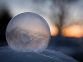 Eine gefrorene Seifenblase liegt auf einer Schneeschicht.