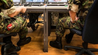Soldaten sitzen an einem Tisch, auf dem mehrere Laptops stehen.