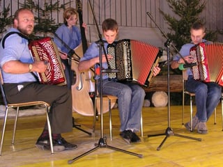 Drei Akkordeonspieler und eine Bassgeigerin beim Musizieren auf einer urchigen Bühne.