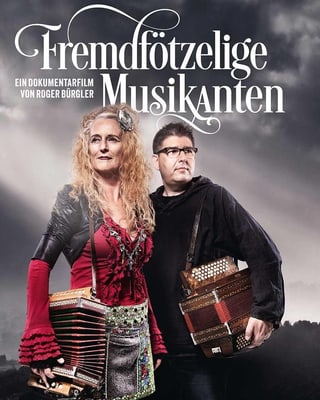 Eine Frau mit blonder Haarmähne und ein dunkelhaariger Mann mit Brille tragen je ein Schwyzerörgeli. Eine Frau mit blonder Haarmähne und ein dunkelhaariger Mann mit Brille tragen je ein Schwyzerörgeli.