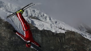 Mann in rotem Anzug mit den Ski in den Luft.
