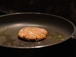 Das Burgerfleisch in einer Bratpfanne, die Würmchen sind in das Fleisch eingearbeitet, sie sind ersichtlich. 