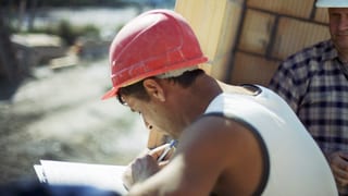 Bauarbeiter mit rotem Helm füllt ein Formular aus. 